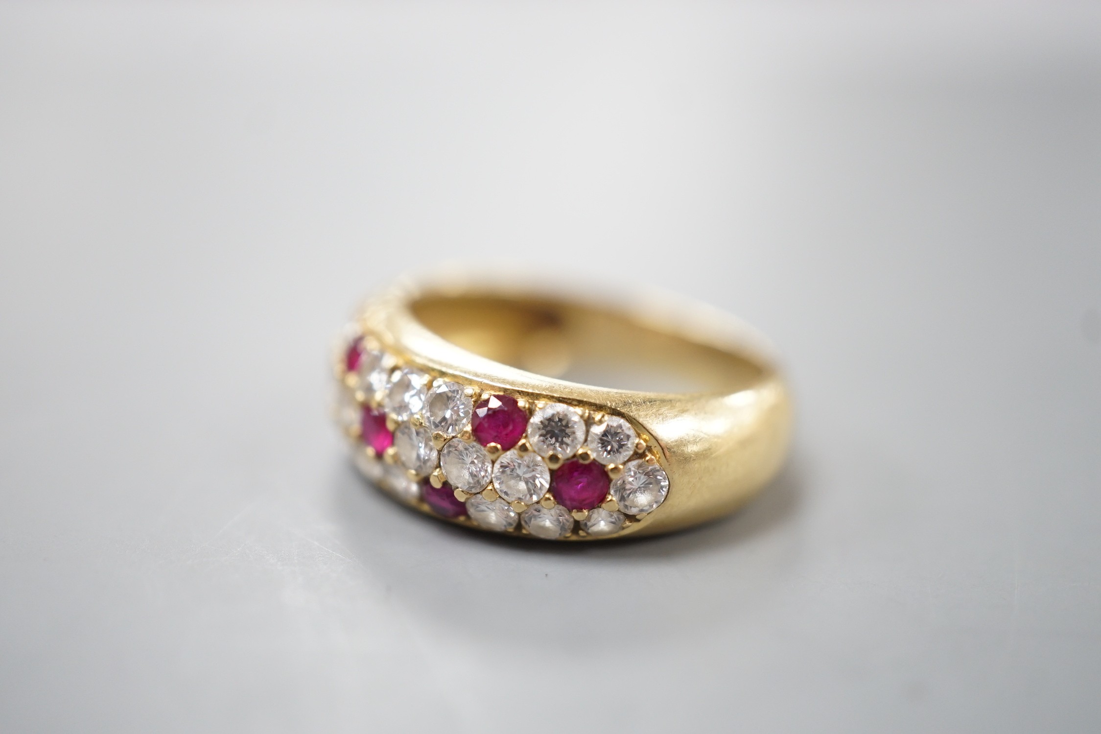 A modern yellow metal, ruby and diamond cluster set half hoop ring, size L/M, gross weight 4.5 grams.